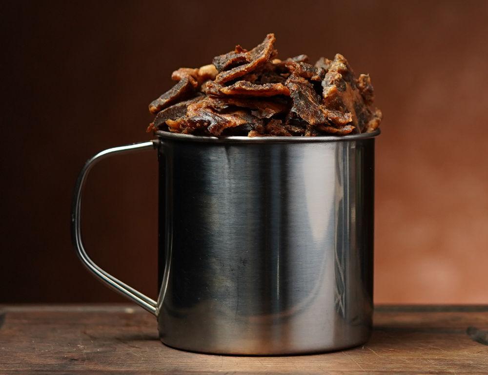 Pork jerky in metalen mok op bruine achtergrond